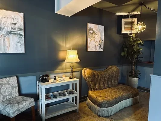 Dark, eclectic lounge featuring vintage phone, patterned chaise, and art.