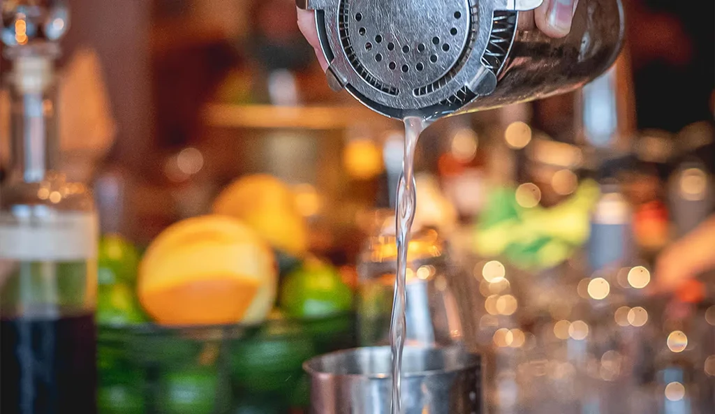 Stainless steel shaker pouring a drink into a metallic glass.