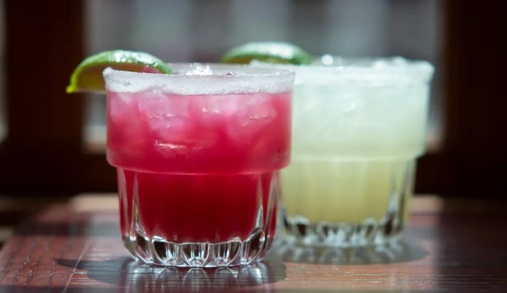 Vibrant magenta and yellow cocktails with ice, lime, and salt rims.