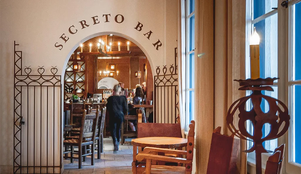 Secreto Bar interior: Arched entrance, wooden tables, warm lighting, people.
