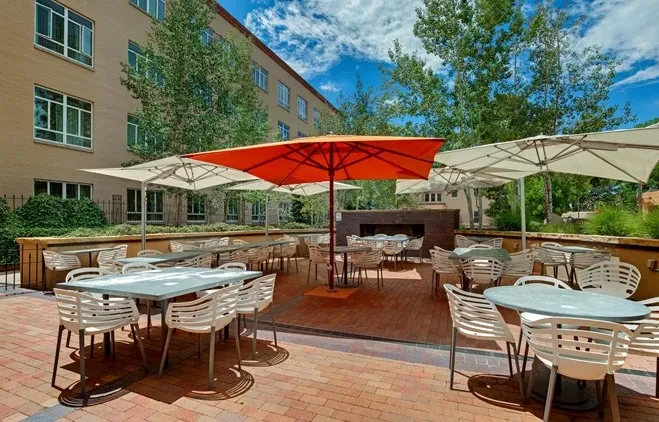 Sunny red-brick outdoor dining patio with white chairs and umbrellas.