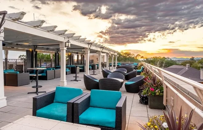 Upscale rooftop patio at sunset with wicker furniture, pergola, and distant landscape.
