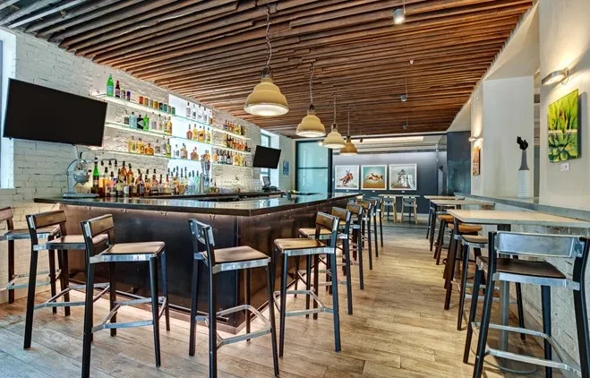 Modern, empty bar interior with backlit shelves, stools, and wooden ceiling.