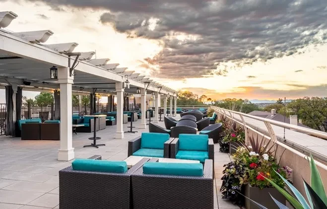 Empty rooftop patio at sunset with teal seating, pergola, and distant mountains.