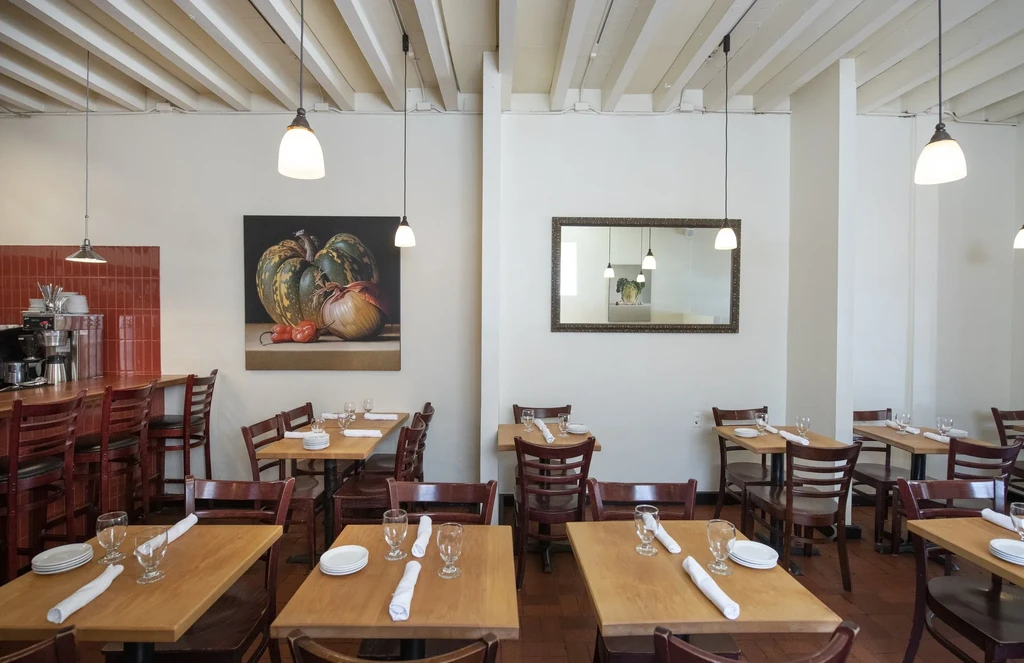 Empty, well-lit restaurant with dining tables, wooden bar, and red tiles.