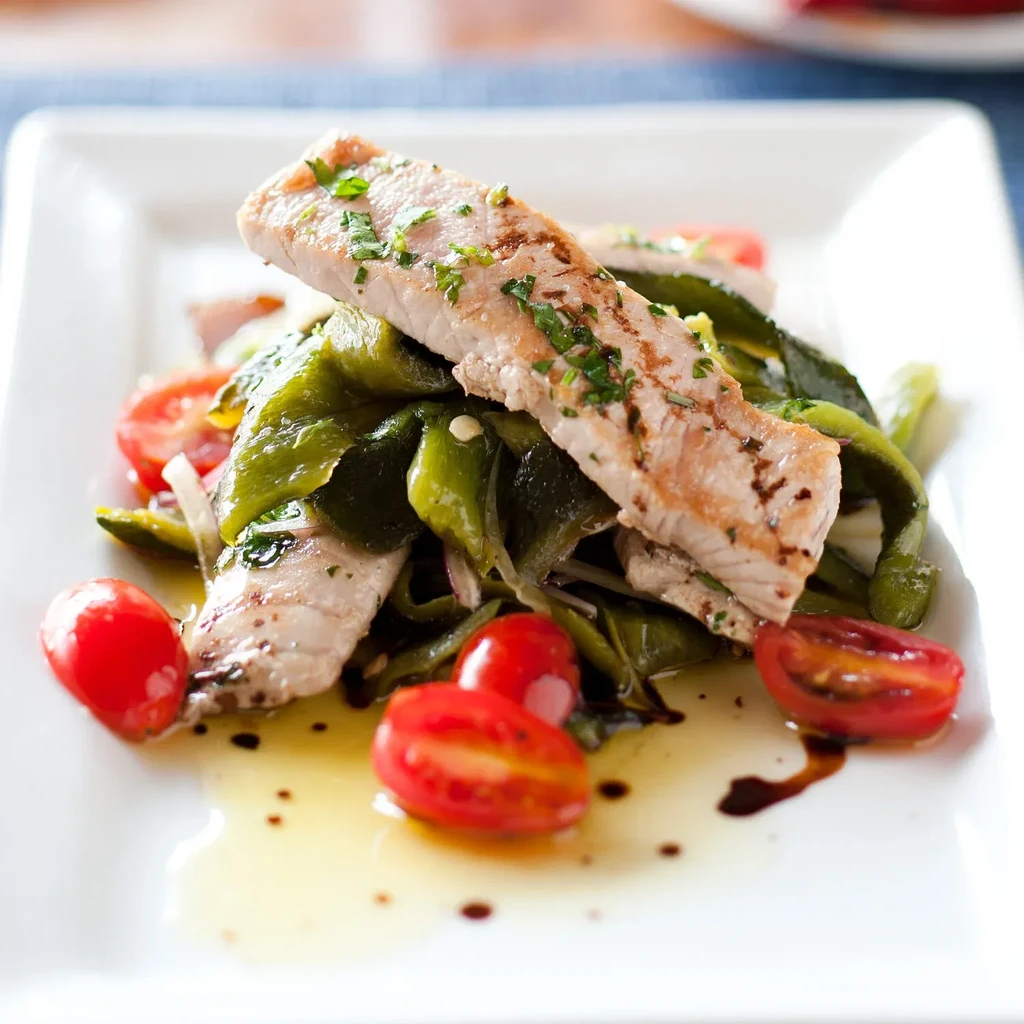 Grilled fish with herbs, peppers, onions, and tomatoes on a white plate.