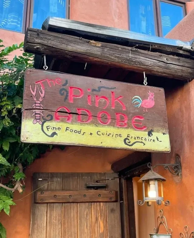 Weathered sign "The Pink Adobe" with lobster and rooster, above a door.