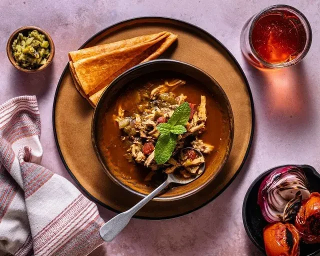 Overhead view of a rustic stew, bread, roasted vegetables, and drink.