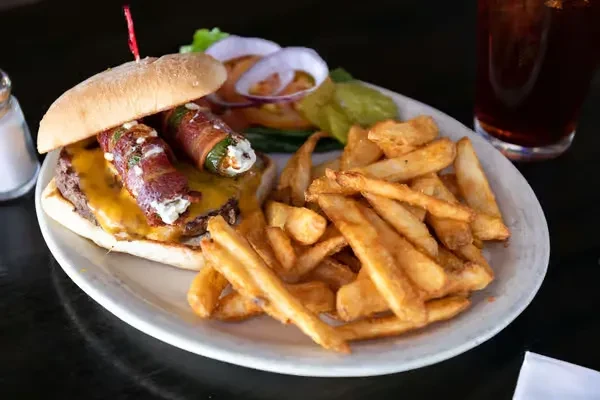 Gourmet burger topped with bacon poppers, served with fries and a pickle.