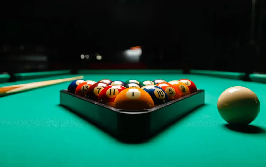 Racked billiard balls, cue ball, pool cue on a green felt table.