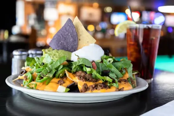 Nachos with meat, cheese, guacamole, upright purple and beige chips, and drink.