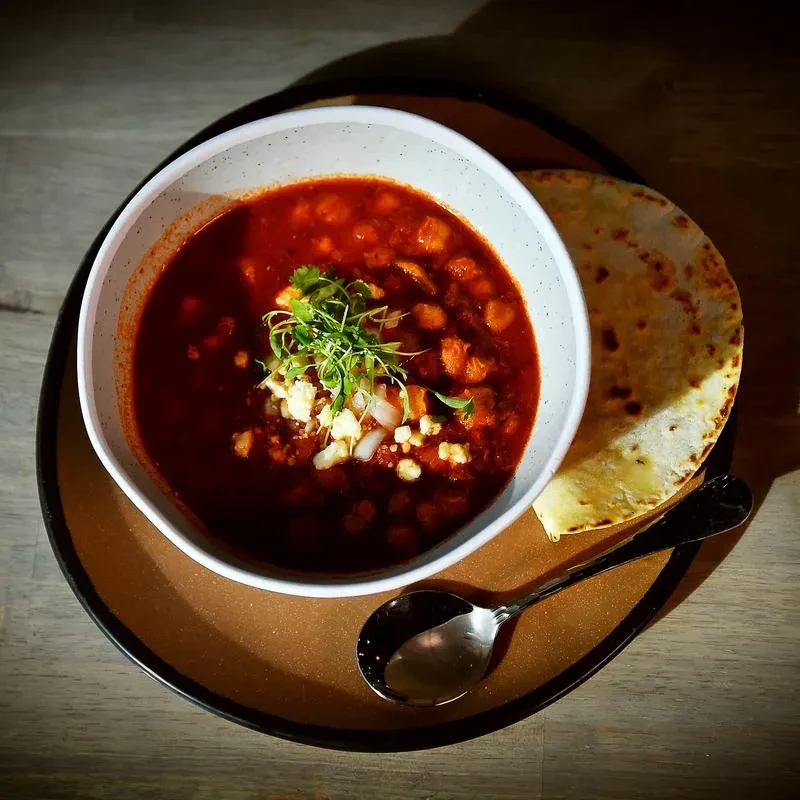 Close-up of a garnished reddish-brown stew, flatbread, and spoon.