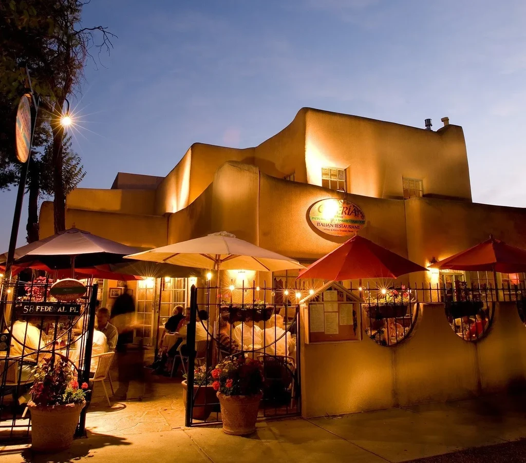 Golden-lit adobe Italian restaurant with outdoor patio and diners at dusk.