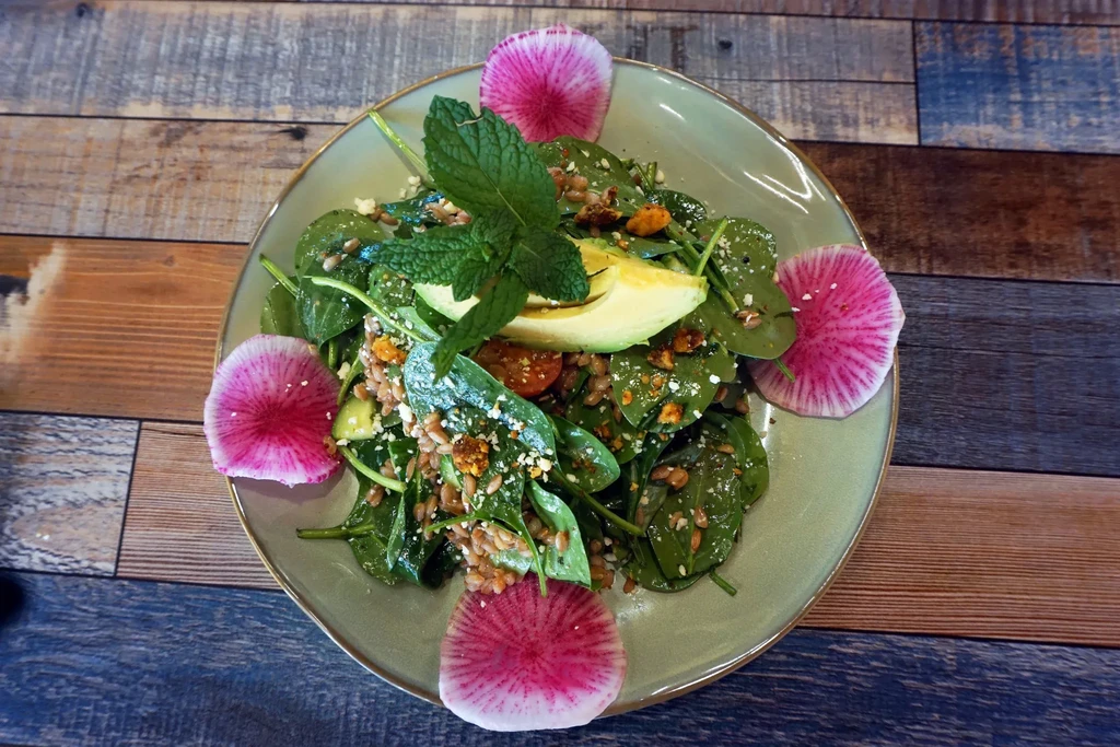 Fresh spinach salad with avocado, radishes, and tomatoes on a wooden table.