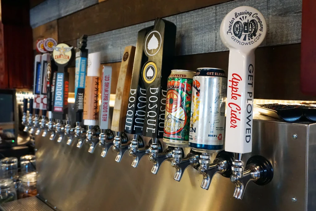 Row of various craft beer tap handles and branded beverage cans.