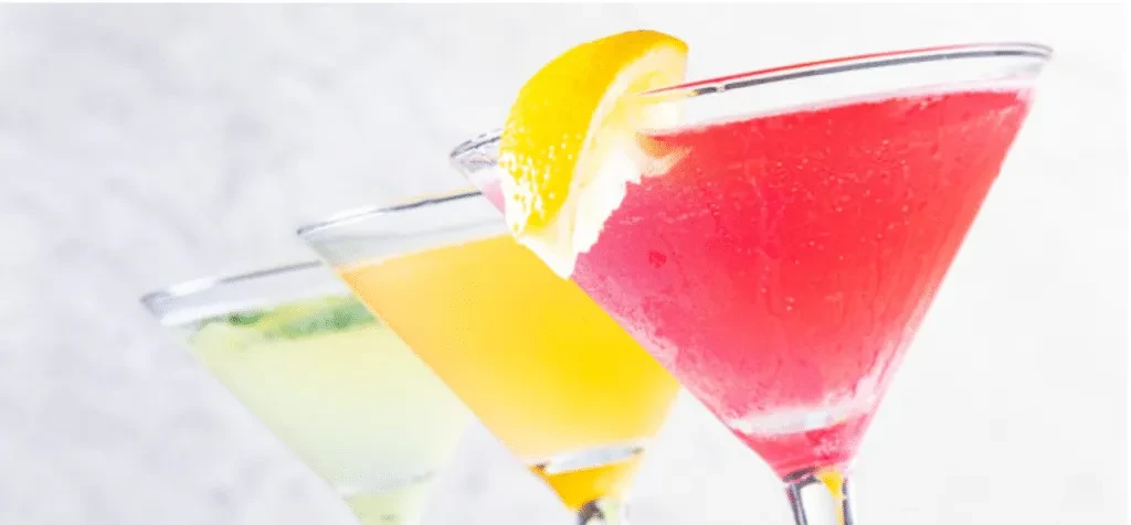 Three colorful cocktails in martini glasses: red, yellow, green.