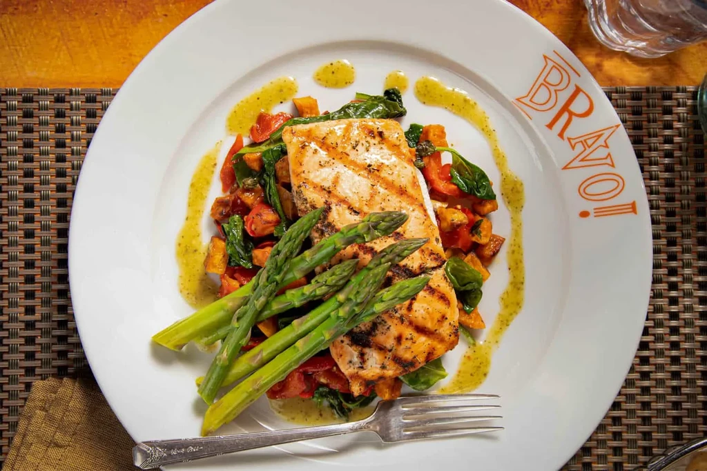 Grilled salmon with asparagus, roasted vegetables, and sauce on a Bravo plate.