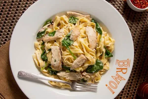 Plate of creamy chicken fettuccine and spinach pasta with a fork.