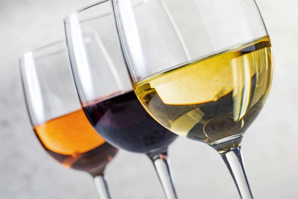 Three wine glasses with red, orange, and white wines.