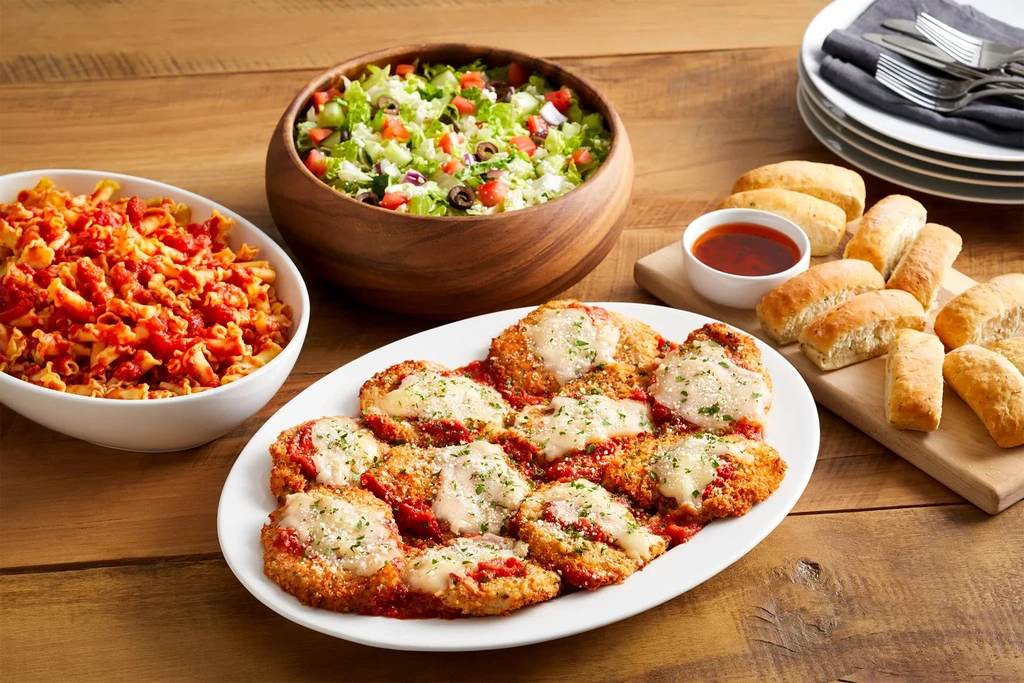 Italian dinner spread with chicken parmesan, pasta, green salad, and breadsticks.