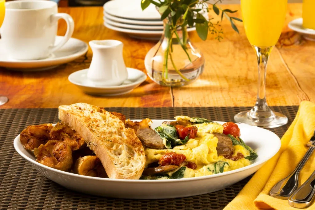 Breakfast plate of eggs, plantains, toast, and sausage on rustic wood.