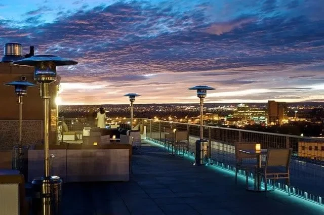 Rooftop patio at dusk, glowing heaters overlook city skyline.