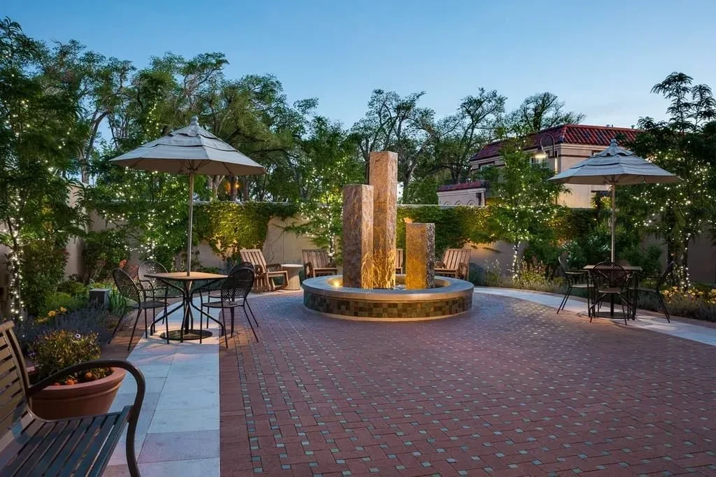Outdoor patio with stone fountain, dining tables, and string lights at dusk.