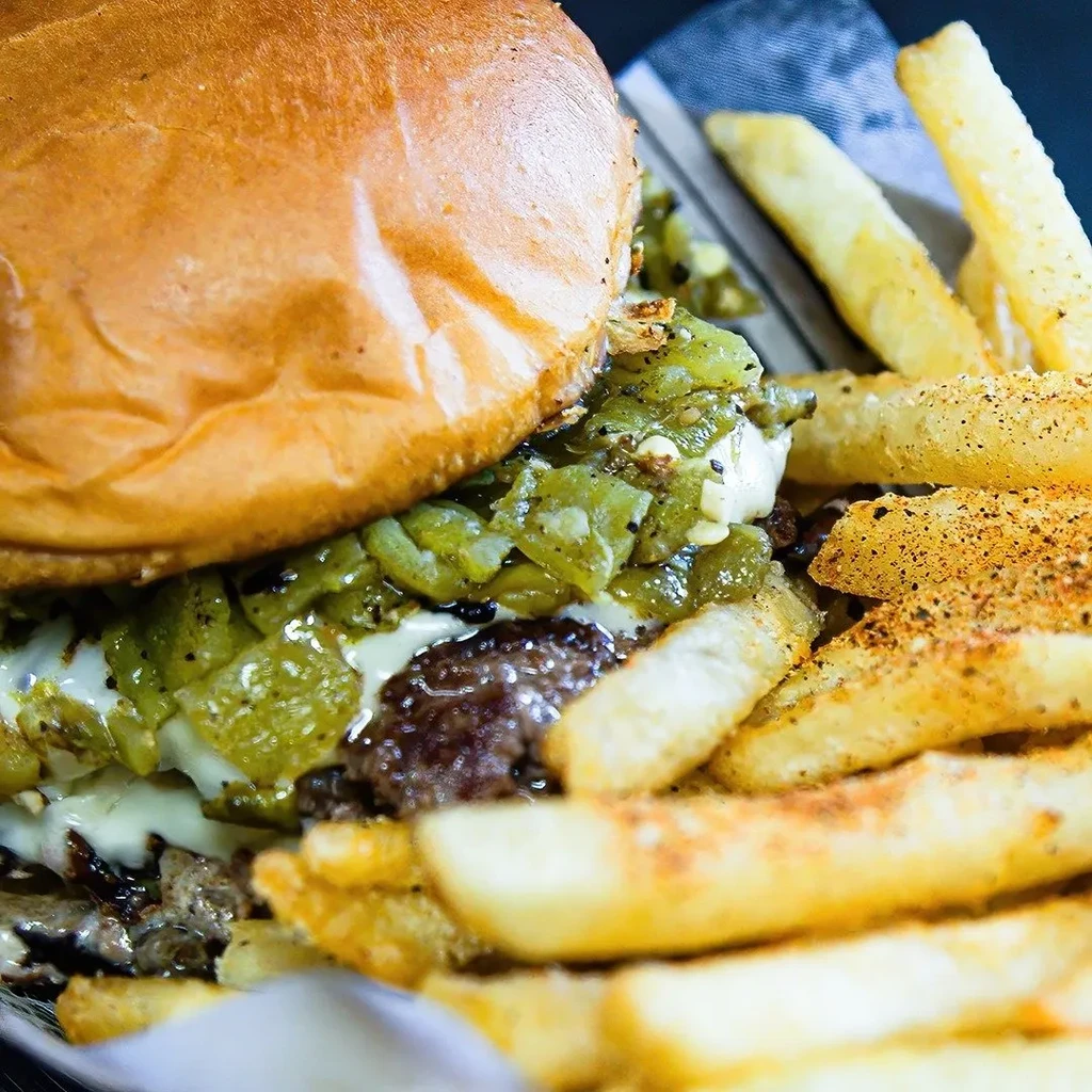 Burger with melted cheese, green topping, and seasoned thick-cut fries.