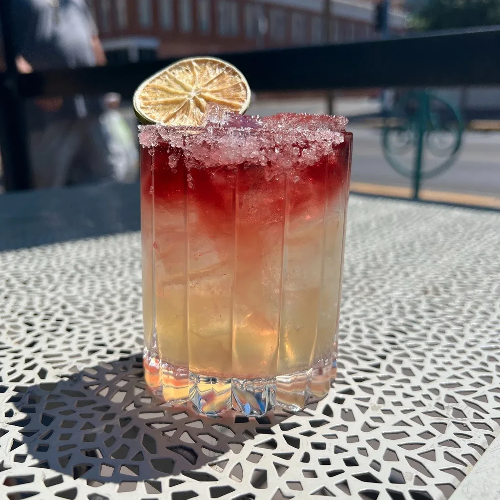 Layered red-yellow cocktail with sugared rim and lime garnish.