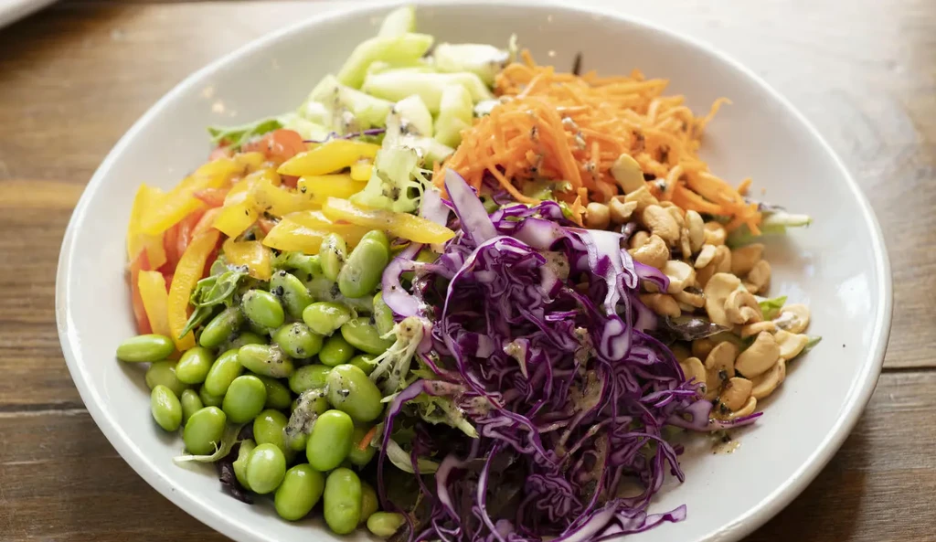 White bowl of colorful salad with edamame, cashews, and mixed vegetables.
