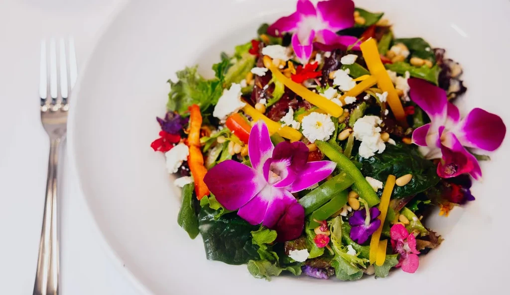Vibrant salad with bell peppers, feta, pine nuts, and purple orchids.