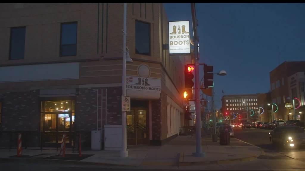 Illuminated 'Bourbon & Boots' building on a city corner at dusk.