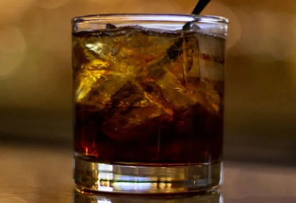 Dark amber drink with ice and a straw in a clear glass.