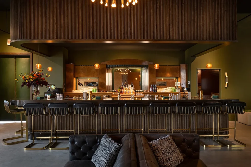 Empty upscale bar with elegant stools, bottles, and ornate mirror.