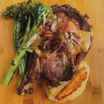 Seared steak, broccolini, mashed potatoes, and crispy chip on rustic wood.