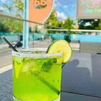 Green cocktail with mint, lime, and cucumber on an outdoor patio.
