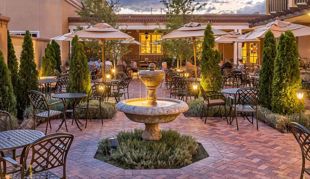 Dusk restaurant patio with stone fountain and many diners.