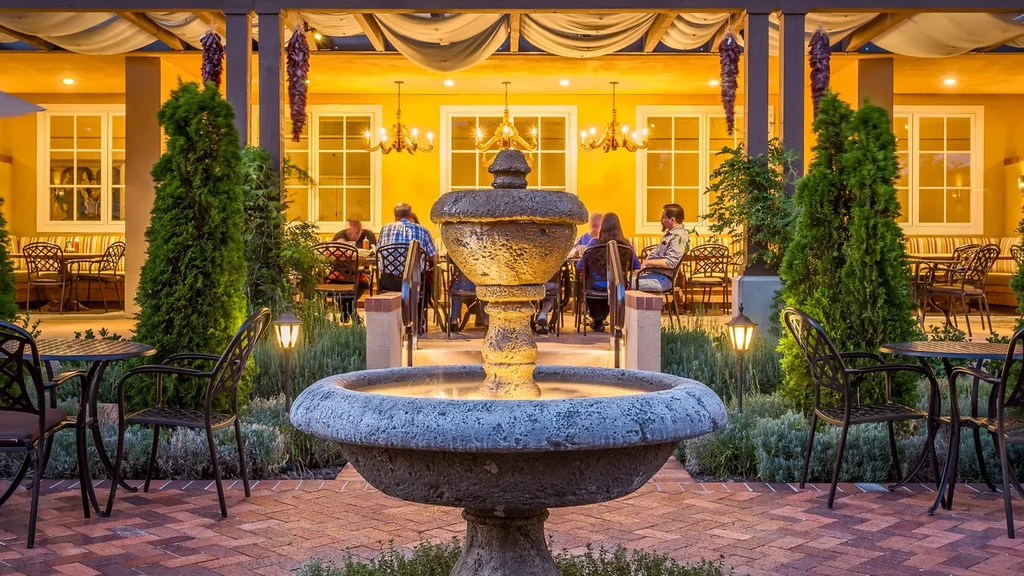 Outdoor restaurant patio with fountain, pergola, and evening diners.