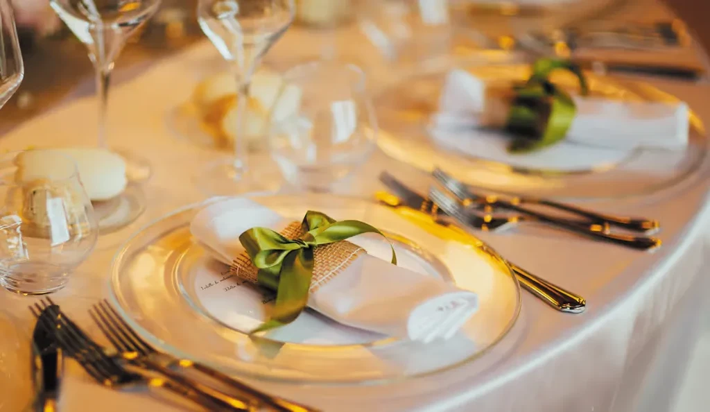Elegant dining place setting with golden cutlery and green ribbon bow.