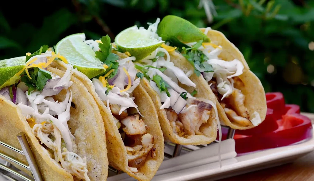 Four fish or chicken tacos in holder with cabbage, cheese, and lime.