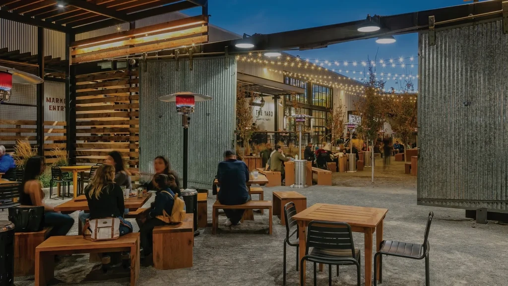 Lively outdoor industrial yard at night with string lights and people.