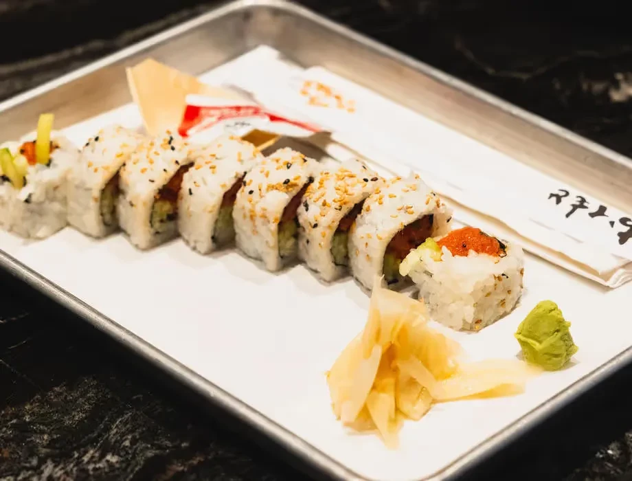 Nine uramaki sushi pieces with roe, sesame, ginger, and wasabi.