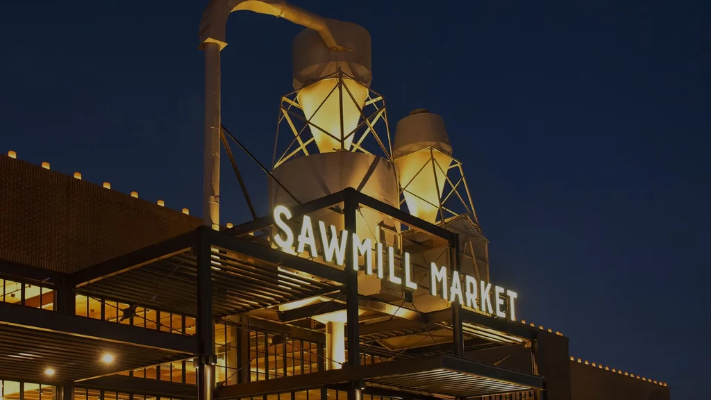 Sawmill Market building at night, illuminated sign, industrial silos above.
