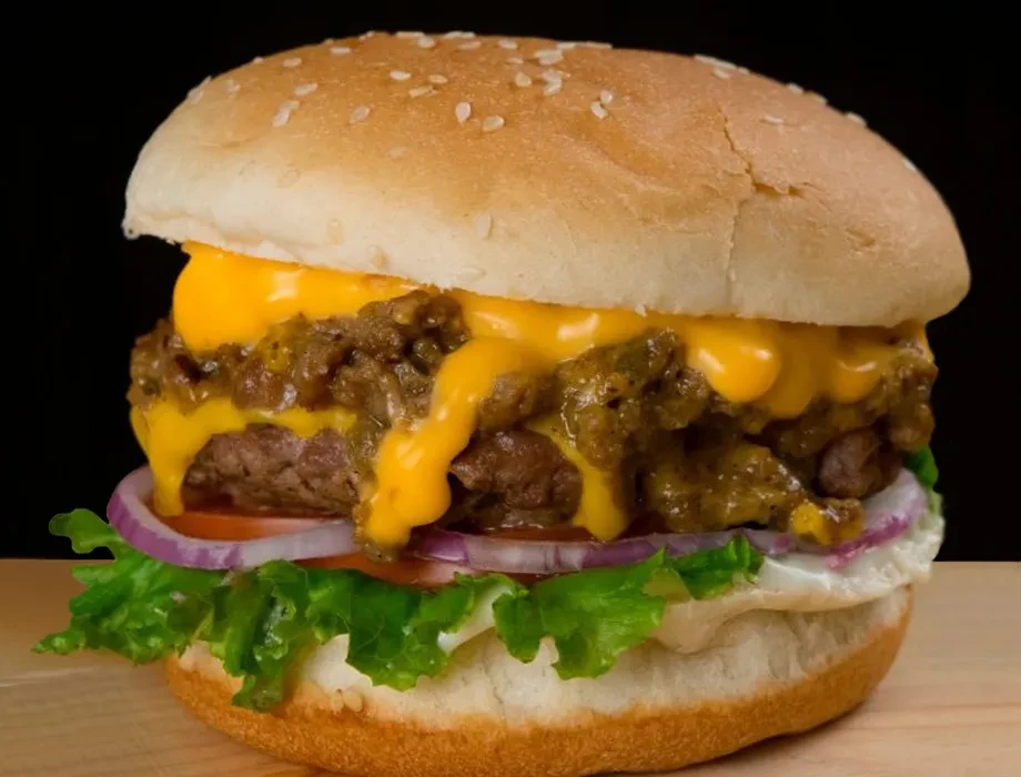 Stacked burger with melted cheese, beef patty, chili, lettuce, and egg.