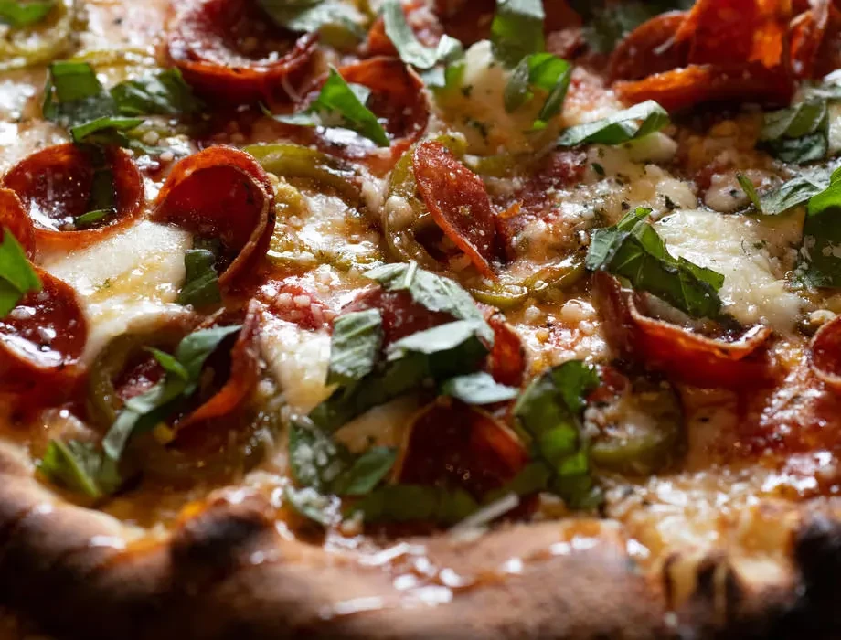 Close-up of baked pizza with pepperoni, mozzarella, basil, and green peppers.
