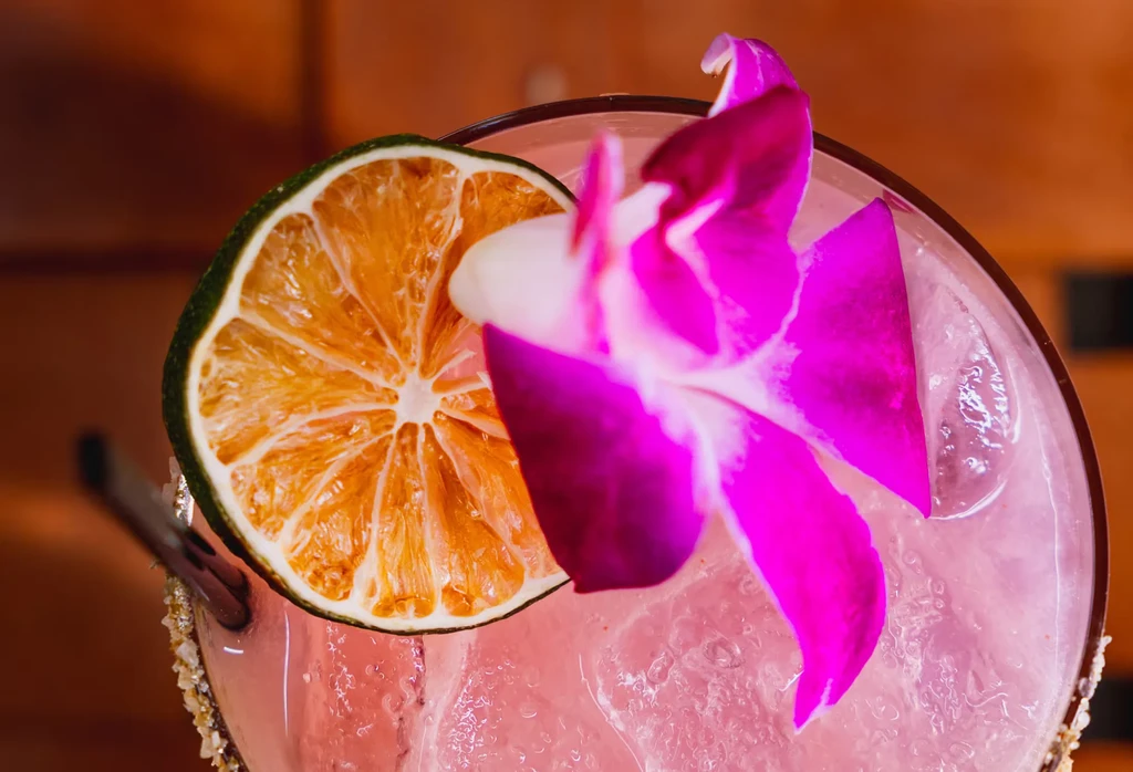 Vibrant pink cocktail with lime slice, orchid, and sparkling rim.