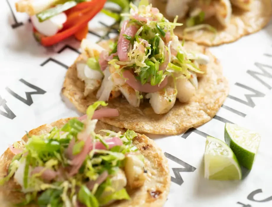 Close-up: three gourmet tacos with shrimp, cabbage, onions, and limes.