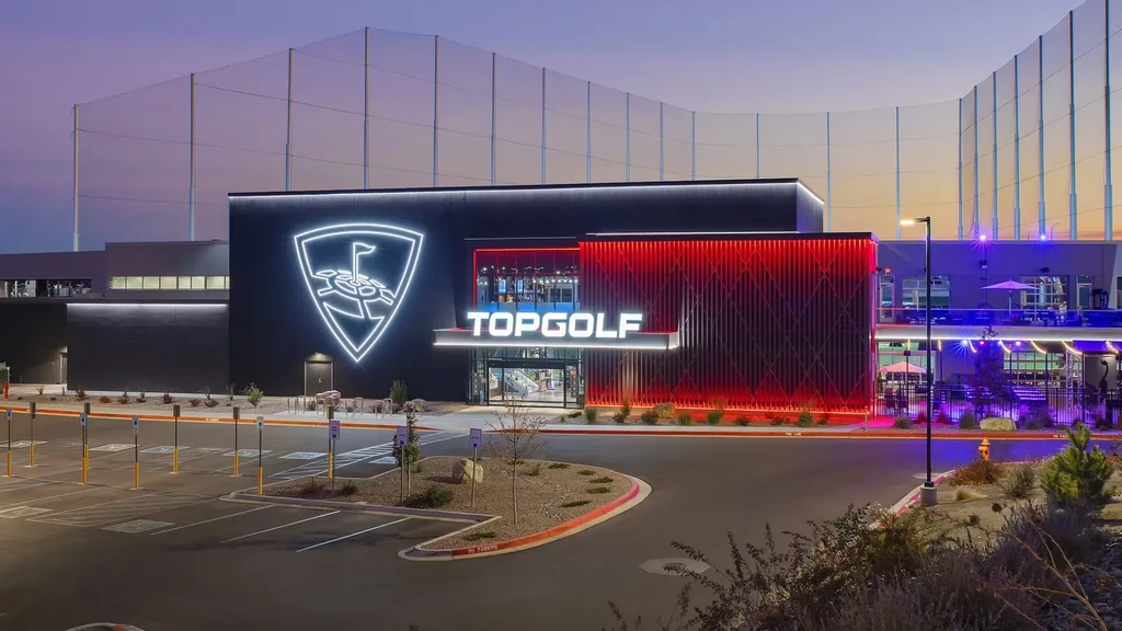 Modern Topgolf venue exterior with vibrant neon lighting at dusk.
