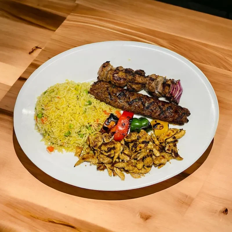 Grilled chicken, meat skewers, yellow rice, and grilled vegetables on a plate.