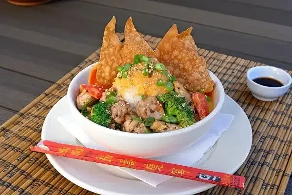 Colorful Asian rice bowl with meat, vegetables, wonton crackers, and chopsticks.